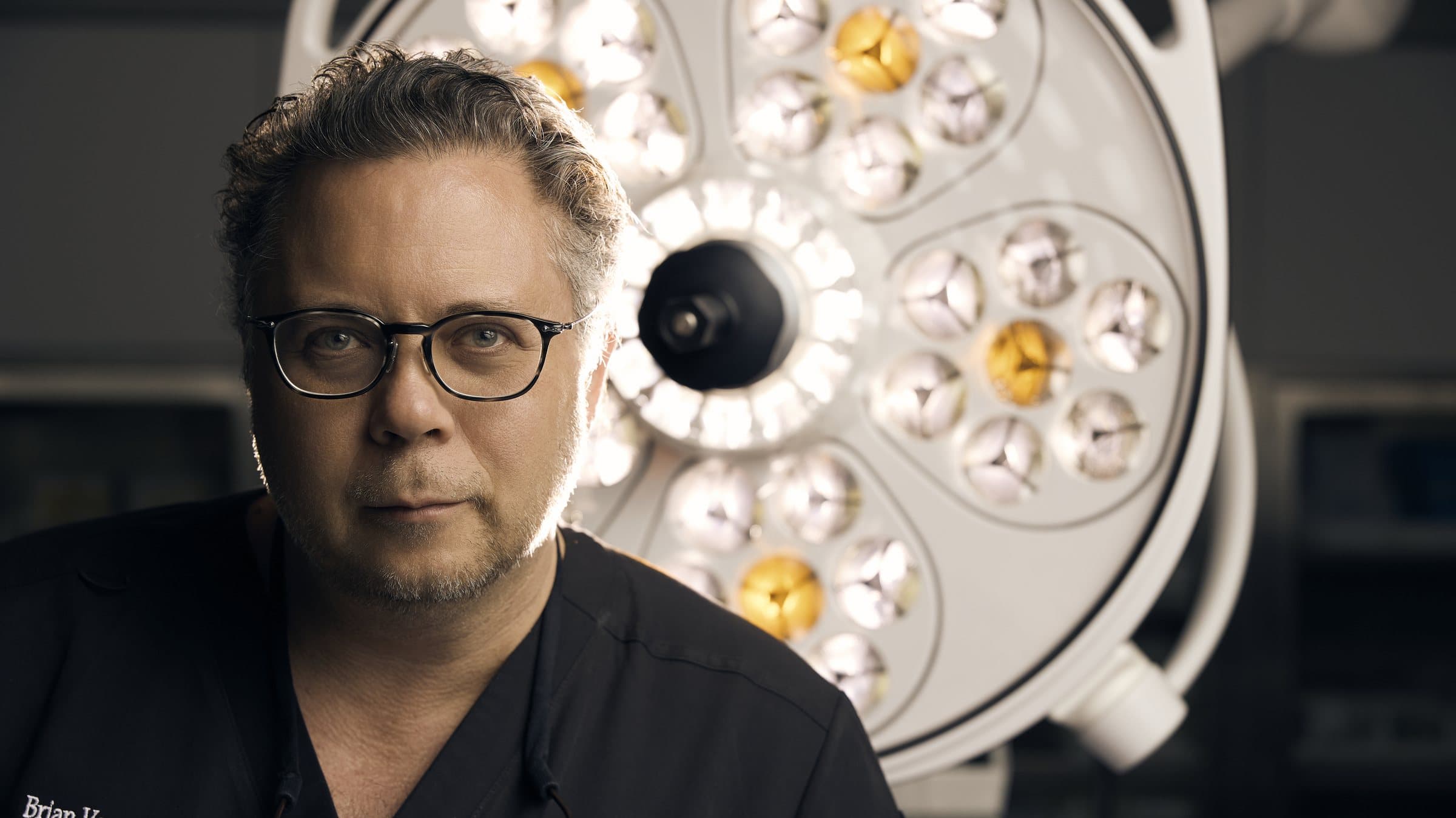 Brian V. Heil, MD, FACS, founder of Acqua Blu Medical Spa, in scrubs beneath a surgical light
