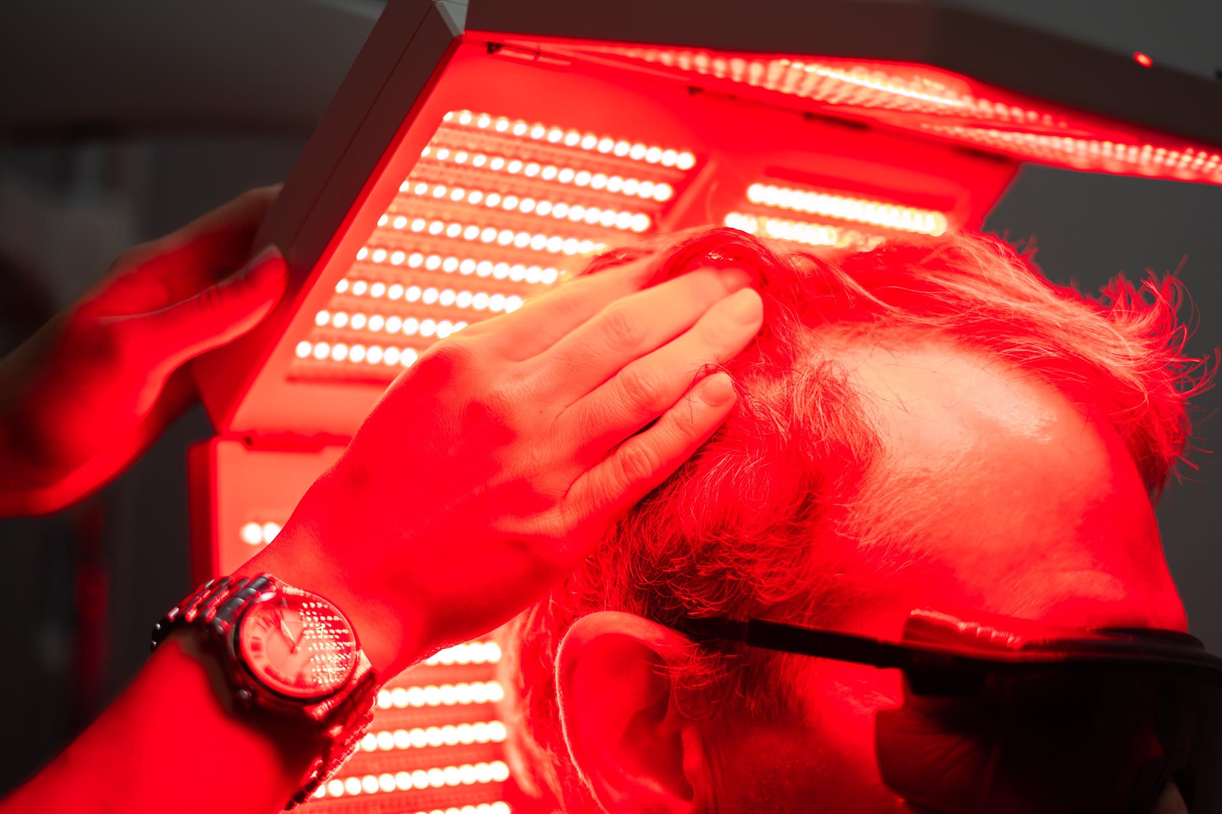 A provider's hands positioning the red LED panel over a patient's head