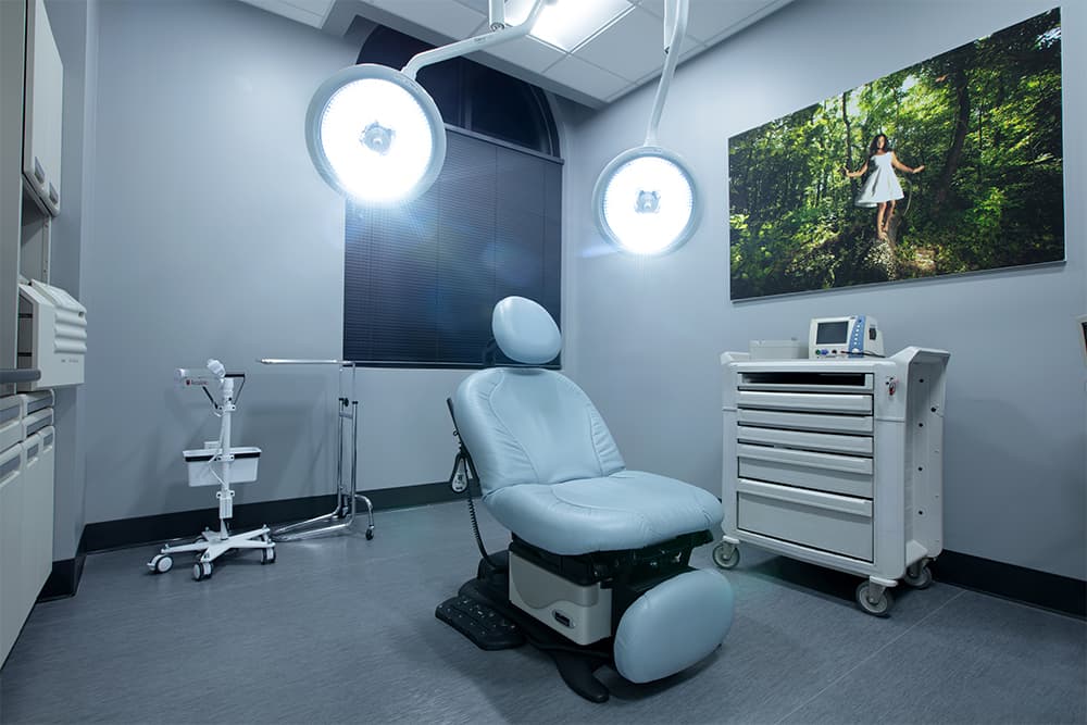 A treatment room with a procedure chair under surgical lights