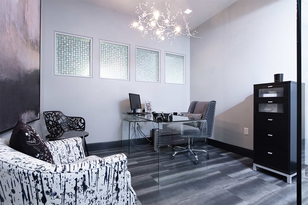 A consultation office at Acqua Blu Medical Spa with a glass desk beneath a chandelier