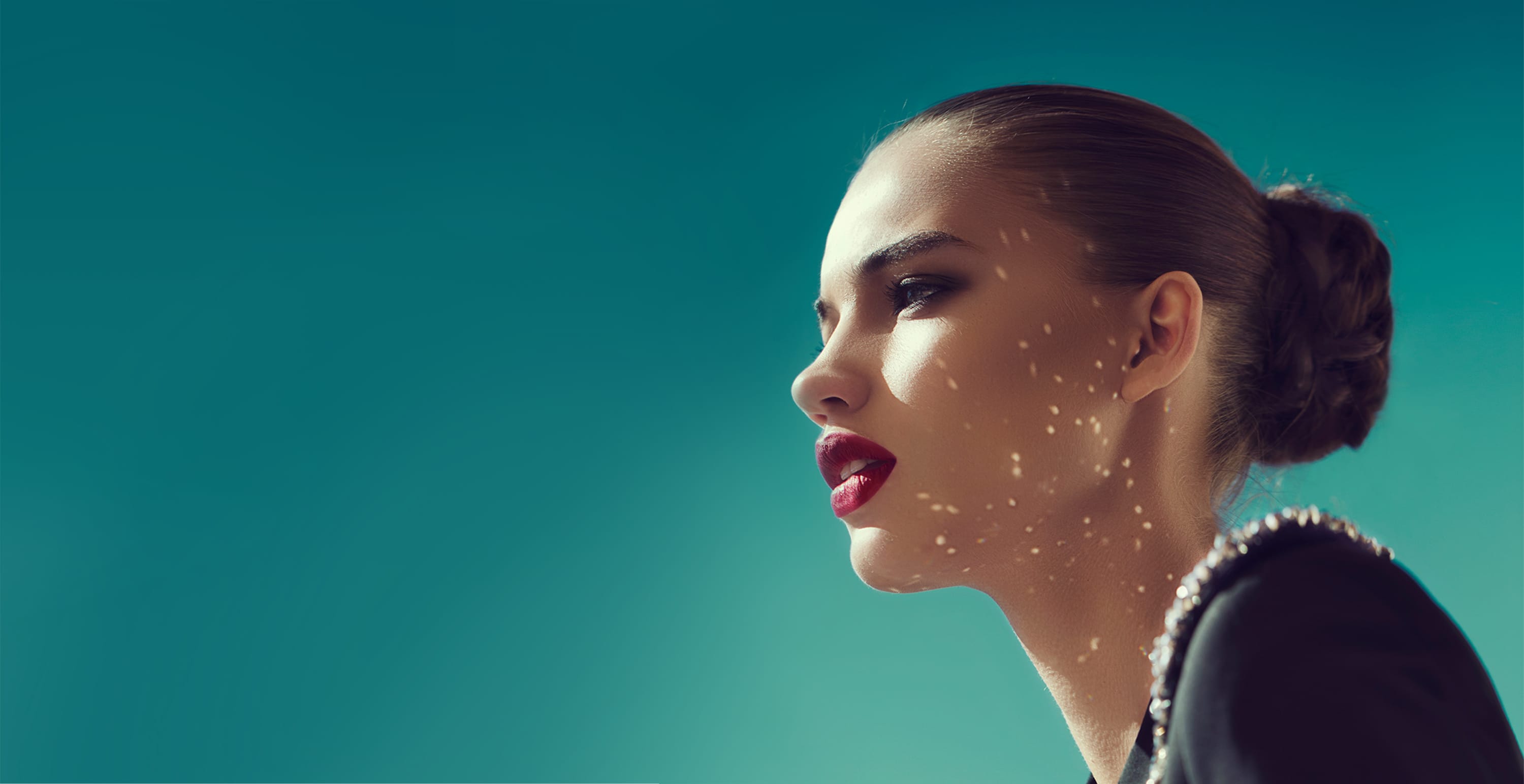 A woman in profile against a deep teal sky, dappled light across her cheek
