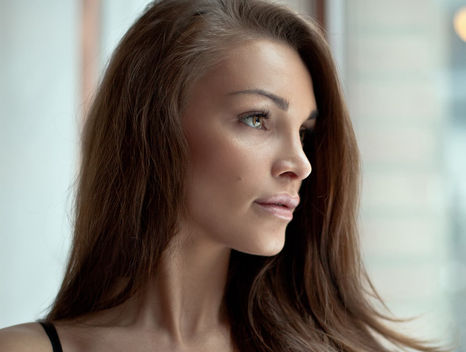 A woman in profile with long brown hair, in soft light